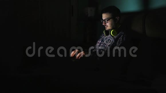 年轻人戴上耳机晚上在笔记本电脑上工作视频的预览图
