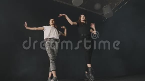 两个年轻漂亮的女人在黑暗工作室训练同步舞蹈编排视频的预览图