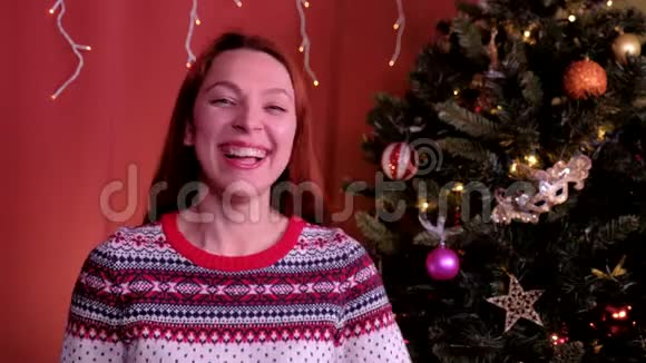 一个红头发的年轻女人看着相机笑着看圣诞节背景中的圣诞树概念视频的预览图