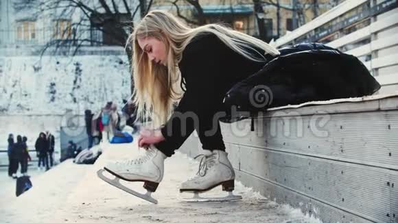 一个金发的年轻女子在走在溜冰场前把自己的花样滑冰绑起来视频的预览图