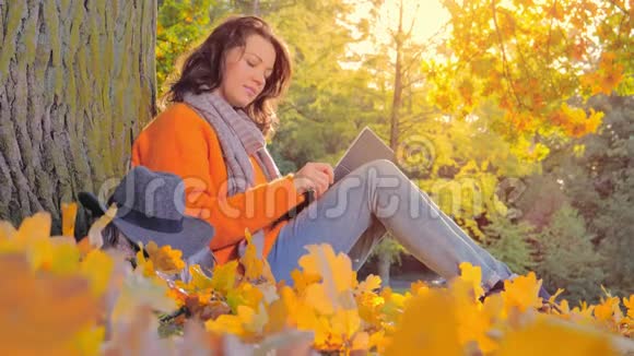 美丽的女人用笔记本电脑工作在秋天公园戴帽子视频的预览图