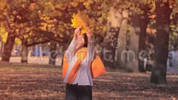 年轻女子带着一束黄色的秋叶享受秋叶的飘落视频的预览图