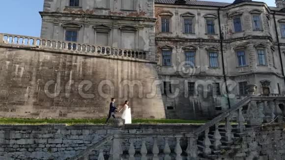 快乐的新婚夫妇在公园的城堡背景上表演一支舞蹈新婚快乐的一家人在婚礼上跳舞视频的预览图
