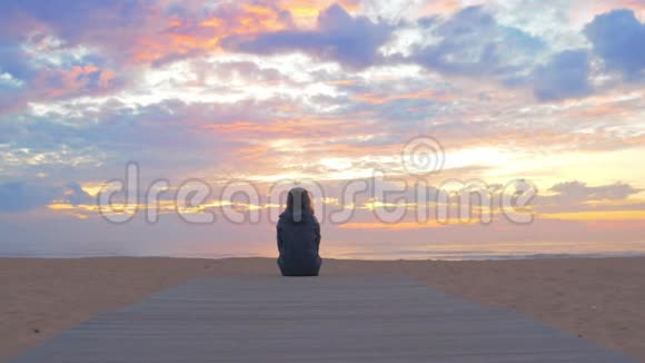 美丽的日落过海女人坐在沙滩上视频的预览图