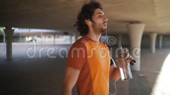 这位年轻的跑步健将耳朵里戴着耳机呼吸急促喝着城里的瓶装水视频的预览图
