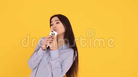 戴着黄色背景耳机的亚洲女孩在电话里唱卡拉OK跳舞视频的预览图
