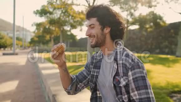 阳光明媚的一天一个年轻人坐在新鲜空气中吃公园里的三明治视频的预览图
