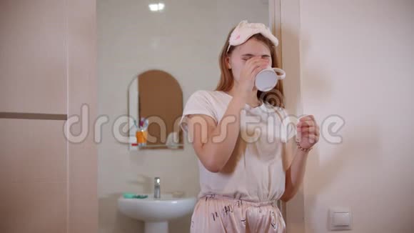 早上一个穿着睡衣喝咖啡的年轻女子站在浴室门口视频的预览图