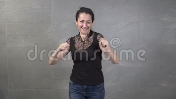 一个甜美的中年东方女人在家中对着灰色的墙壁在镜头前欢快地跳舞她笑摆姿势视频的预览图