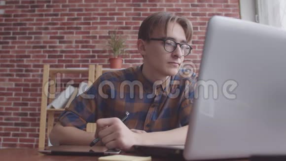 这位网页设计师用一台带有平板电脑的笔记本电脑工作一个头发散乱的家伙用一个图形平板电脑视频的预览图