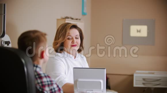 眼科医生治疗成熟的女医生和一个小男孩坐在桌子旁视频的预览图