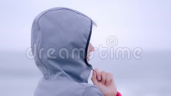 穿着雨衣在灰色的雨滩上享受雨的微笑的女人视频的预览图