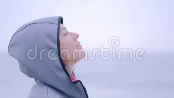 微笑的女人穿着雨衣在灰色的多云海滩上寒冷的一天视频的预览图