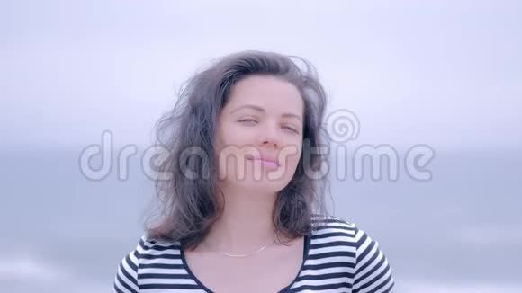 一个蓝眼睛女人在雨天海滩上穿条纹衬衫的肖像视频的预览图