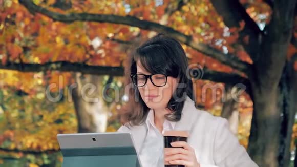 秋天公园的女人喝着咖啡拿着笔记本工作视频的预览图
