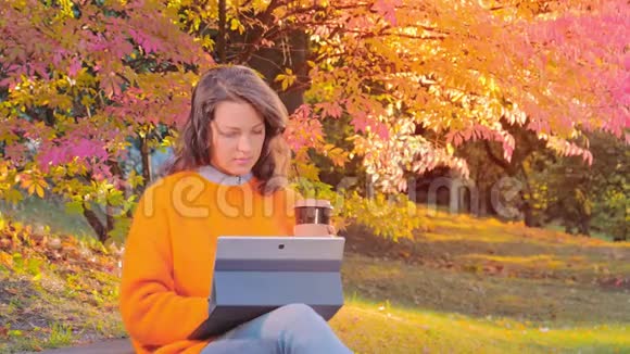 女人拿着笔记本喝着咖啡在公园里享受秋天视频的预览图