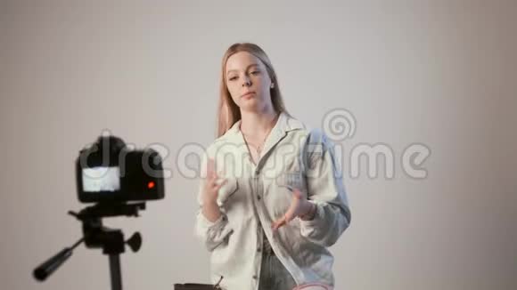 年轻女孩录制视频博客或教程与照片相机连接三脚架视频的预览图