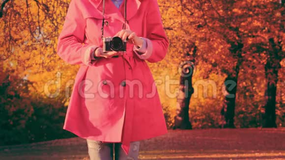 秋天公园里带照相机的时髦女人穿着红色斗篷的时髦年轻女子视频的预览图