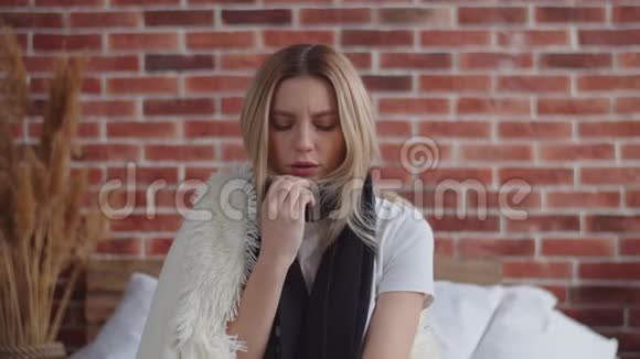 一个漂亮的年轻女人正坐在床上的温暖的毯子下取暖冻僵的女孩揉着肩膀视频的预览图