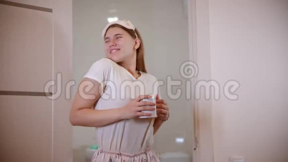 一个年轻的女人微笑着在浴室门口跳舞早上拿着一杯咖啡视频的预览图