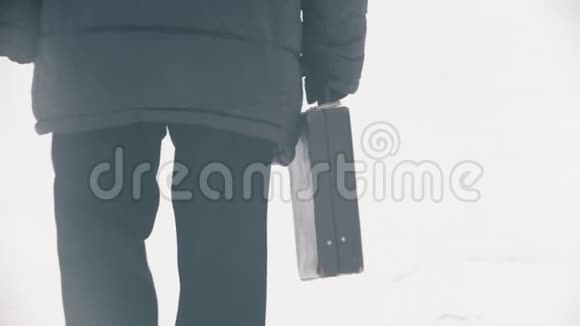 一个穿着羽绒服的老人带着袋子在雪地公园散步视频的预览图