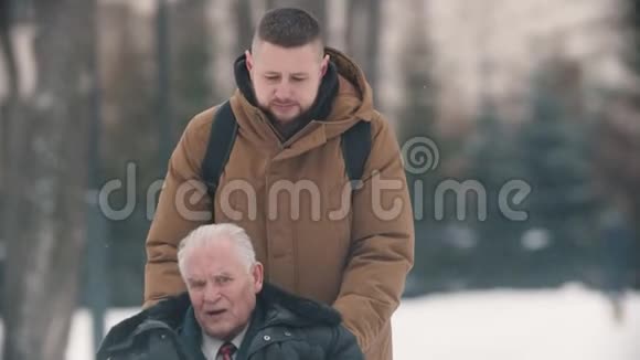 一个年轻人和他的祖父坐轮椅在雪下走在户外视频的预览图