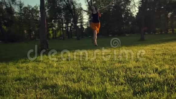 日落时分年轻女子在公园的草地上奔跑跳跃视频的预览图