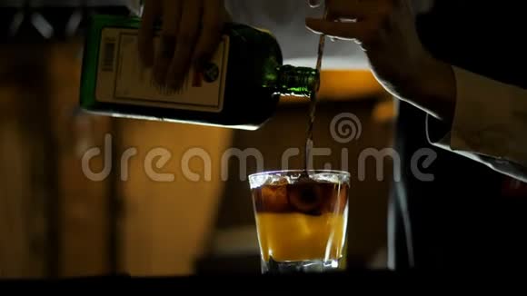 酒保将烈性威士忌倒入酒吧柜台上装有新鲜橙汁的鸡尾酒杯中视频的预览图