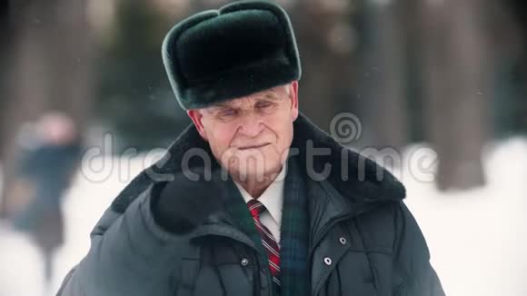 一个微笑着的老人摘下帽子从雪地上把帽子擦干净视频的预览图