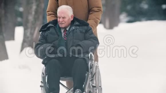 冬天一个年轻人和他的祖父坐轮椅在户外散步视频的预览图