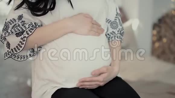 怀孕的年轻女人的手在家里大肚子上奔跑视频的预览图