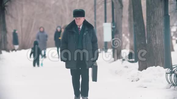 一个独自一人的老人带着袋子在雪地公园散步视频的预览图