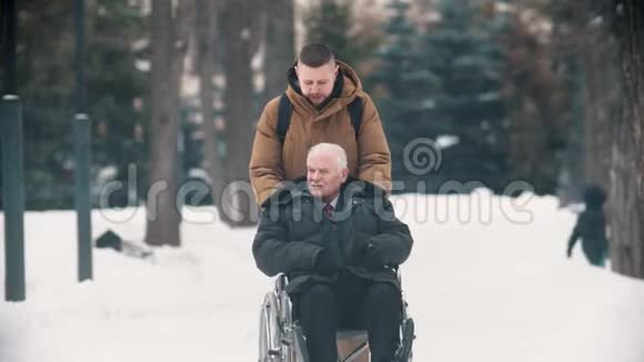 一个年轻人和他的祖父坐轮椅走在户外视频的预览图
