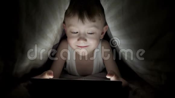 小男孩躺在毯子下玩平板电脑看动画片视频的预览图