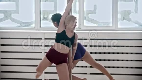 在工作室接受钢管舞训练的女人两个女人在一根钢管上旋转视频的预览图