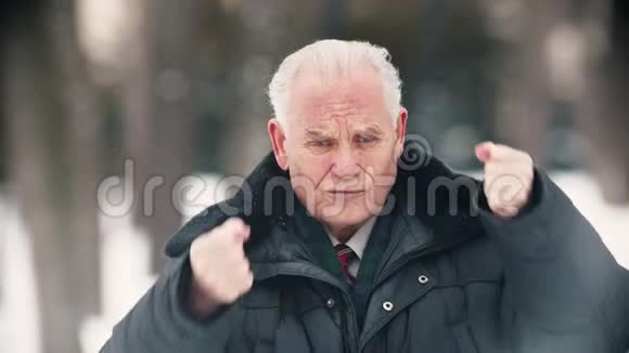 一位老人站在户外下雪时举起双手视频的预览图