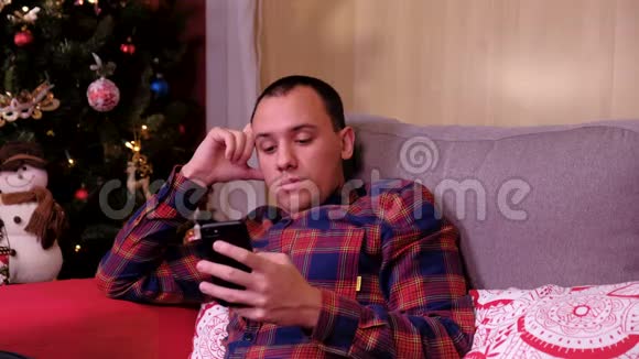一个孤独悲伤的人坐在圣诞树附近拿着手机的肖像假期及新年的概念视频的预览图
