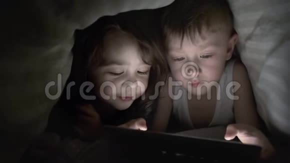 男孩和女孩躺在毯子下玩平板电脑看动画片视频的预览图