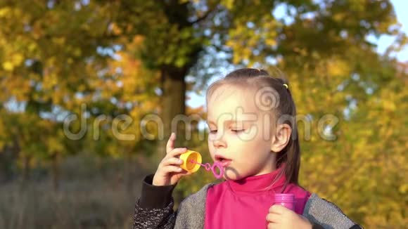 漂亮的小女孩吹肥皂泡在秋天的公园里玩视频的预览图