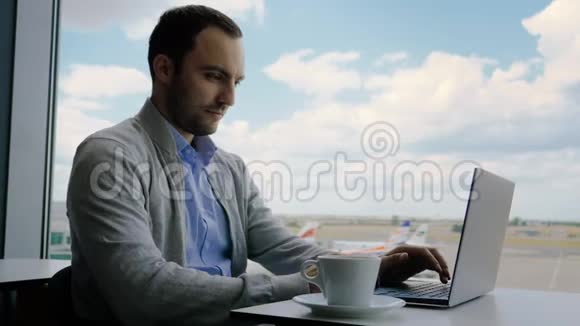 商人在机场候机室用笔记本电脑工作时检查他的手机视频的预览图