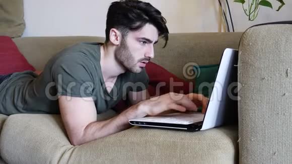 年轻人在沙发上做笔记本电脑作业视频的预览图