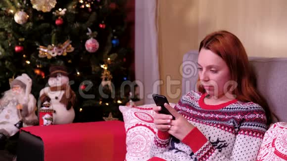 一个孤独悲伤的女人坐在圣诞树旁用手机的肖像假期和新年的概念视频的预览图