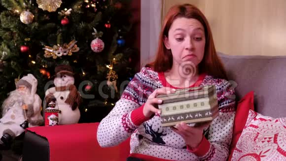 圣诞礼物悲伤的女人躺在圣诞树附近的沙发上打开礼物失望和不开心概念视频的预览图