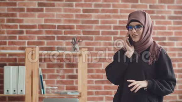 一个戴头巾的年轻女人在打电话穆斯林女孩在办公室的智能手机上交流视频的预览图