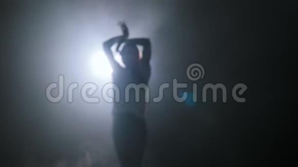 年轻女子双手在黑暗的工作室里跳舞的剪影视频的预览图