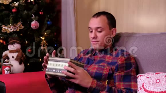 圣诞礼物悲伤的人躺在圣诞树附近的沙发上打开礼物失望和不开心概念视频的预览图