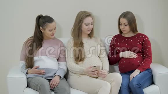 怀孕的女孩在候诊室等医生时看着电话视频的预览图