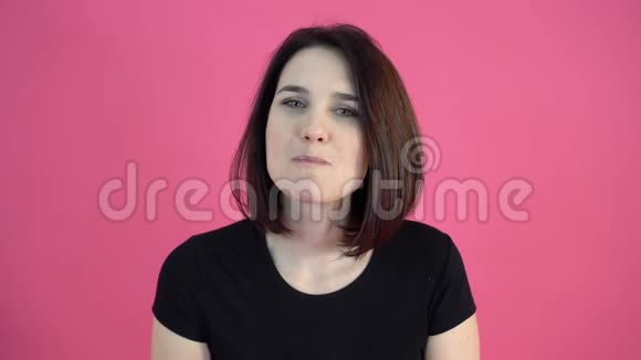 年轻漂亮的女孩一双绿色的眼睛穿着一件黑色T恤黑发女人用口香糖吹出一个大泡泡在粉红色的bac上微笑视频的预览图