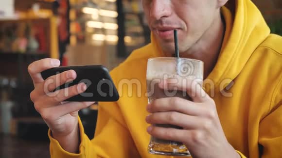 在现代咖啡馆里用智能手机触摸屏关闭男人男性饮用奶昔或冰沙并在智能手机上发短信视频的预览图