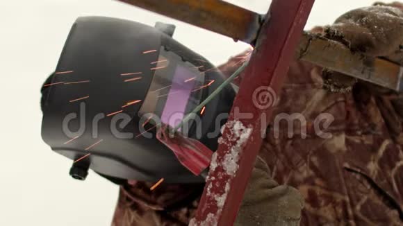 一个穿暖和西装的专业人士工作手套和焊接面罩在冬天焊接金属框架视频的预览图